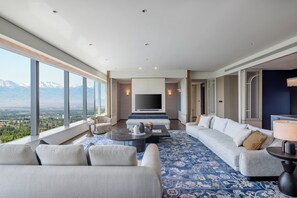 Une chambre d’hôtel moderne dotée d’une grande fenêtre donnant sur les montagnes, d’un canapé, d’une table basse et d’un téléviseur.
