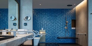 Une salle de bain moderne avec un mur orné d’un motif bleu, un grand miroir, une baignoire et des toilettes.