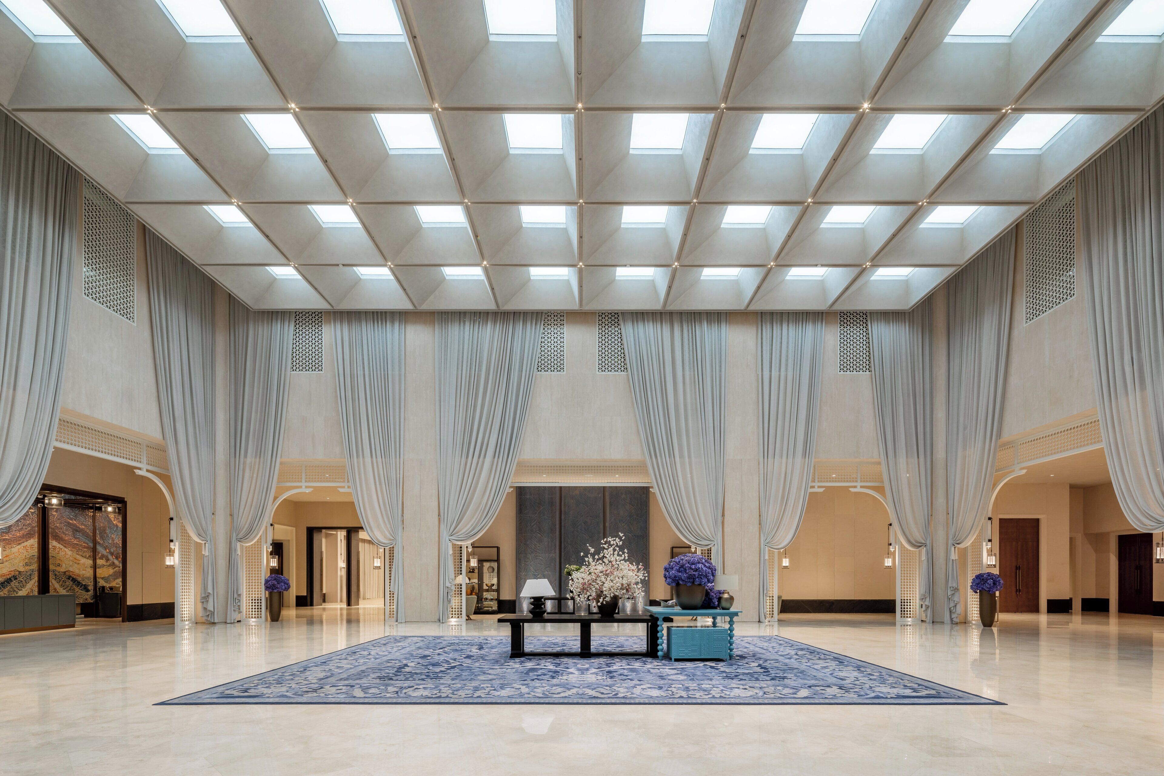 Un hall d’entrée spacieux, doté d’un haut plafond, de grandes fenêtres et d’un espace central avec une table et des chaises.