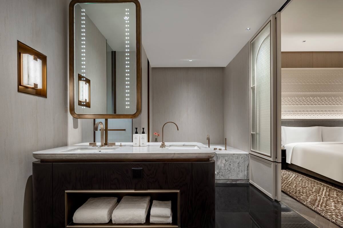 A modern bathroom with a large mirror, dual sinks, and a vanity with a built-in shelf for towels.