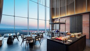 A modern restaurant with a panoramic view, featuring a dining area with tables and chairs, a buffet counter with various food items, and a large window offering a scenic view. - InterContinental Yining by IHG (Yining)