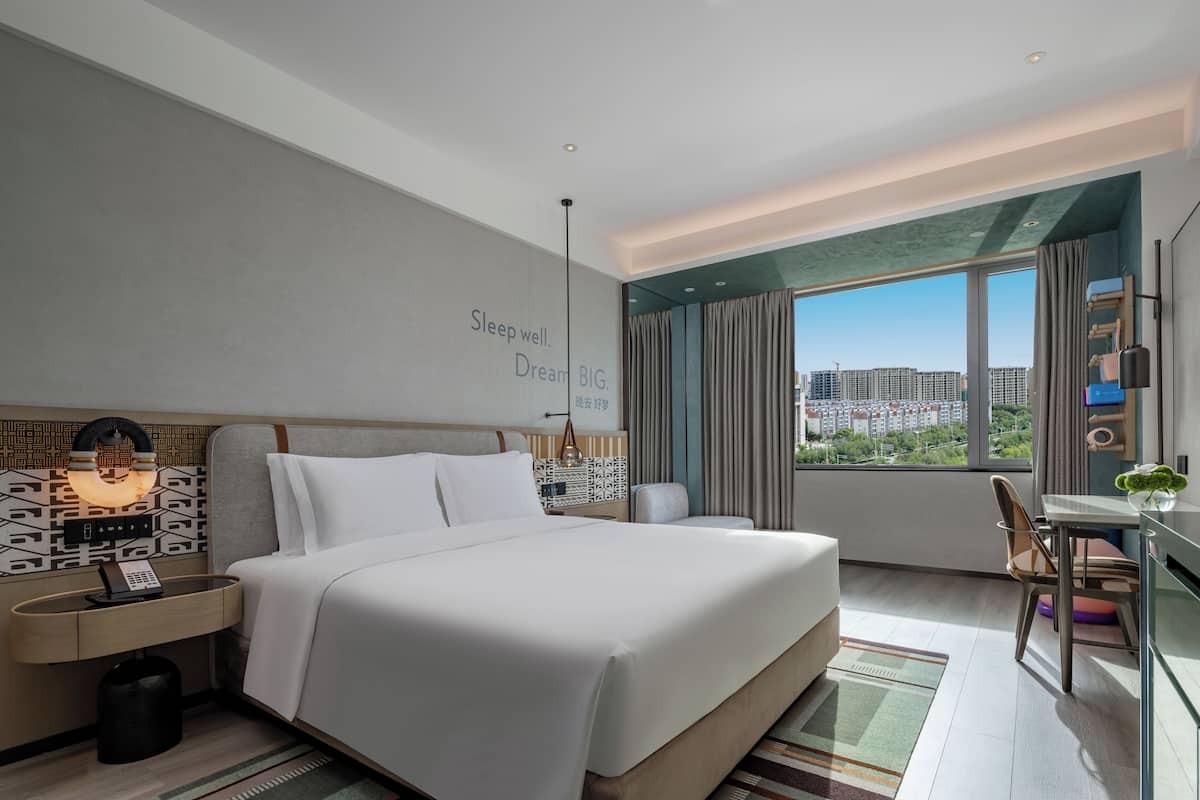 A modern hotel room with a large bed, a desk, and a view of the city.
