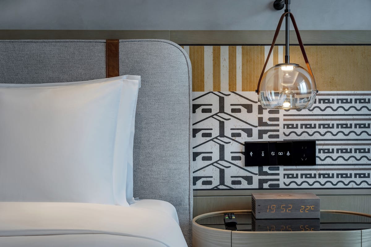 A modern hotel room with a grey sofa, a white pillow, a wall clock, and a decorative wall panel.