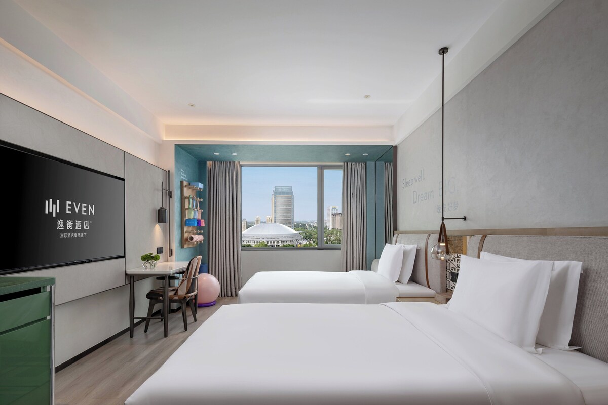 Une chambre d’hôtel avec un lit, un bureau, une télévision et une vue sur le paysage urbain.