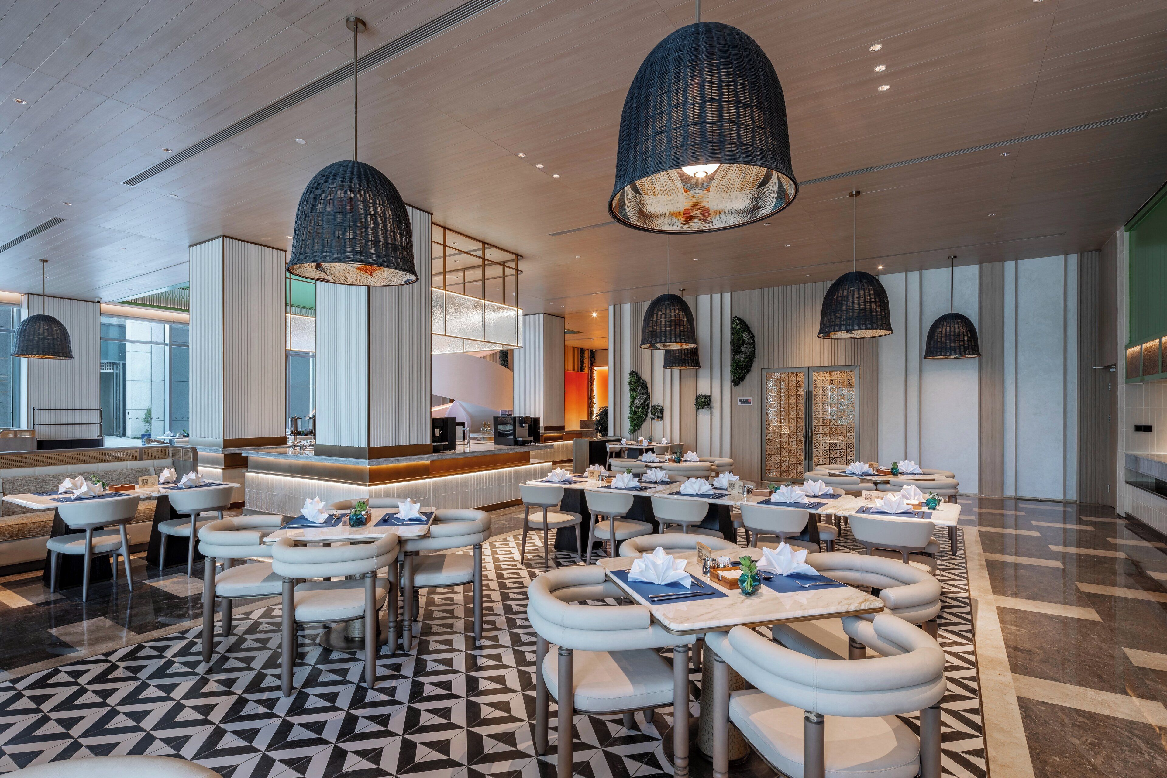 A modern restaurant with round tables and chairs, pendant lighting, and a geometric floor pattern.
