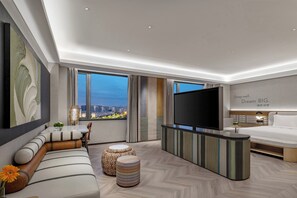 A modern hotel room with a large bed, a flat-screen TV, a sofa, ottomans, and a city view. - EVEN Hotel Yining by IHG (Yining)