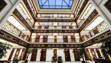 Un atrio de varios niveles con techo de cristal, balcones de madera y plantas en macetas.