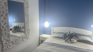 A bedroom with a white ornate mirror, a bed with striped bedding, and a hanging light fixture.