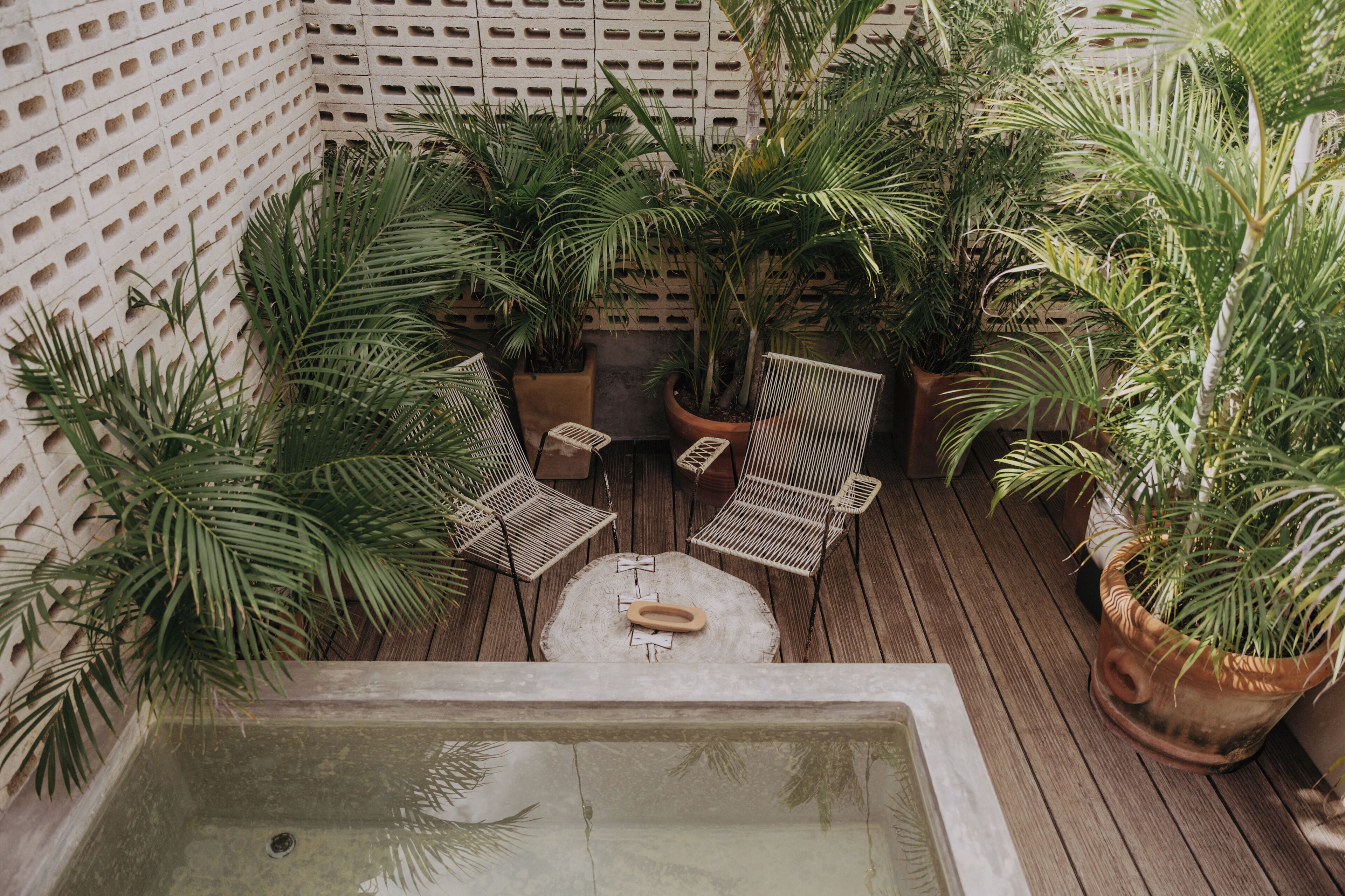 A wooden deck with a hot tub, surrounded by potted plants and wicker chairs.
