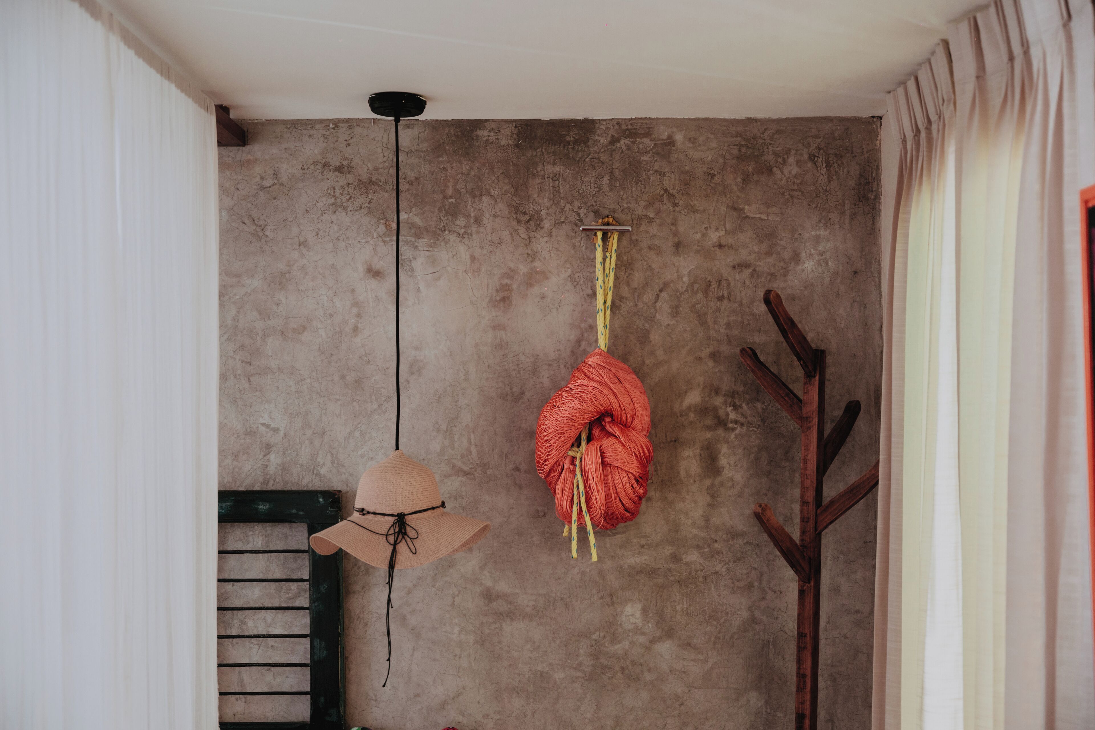 Ein Zimmer mit einer Betonwand, einem hölzernen Kleiderständer und einem an der Wand hängenden Hut.