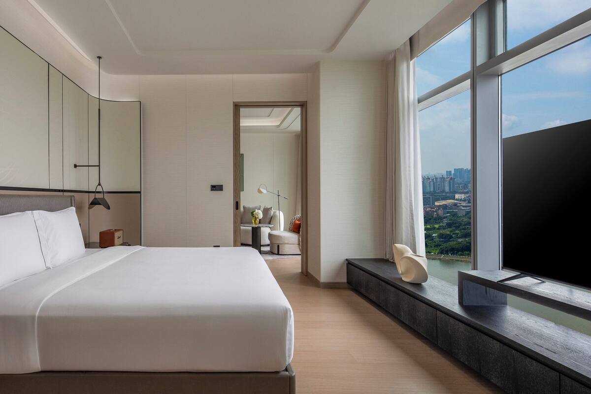 Ein modernes Hotelzimmer mit einem großen Bett, einem Fernseher und Blick auf die Stadt.