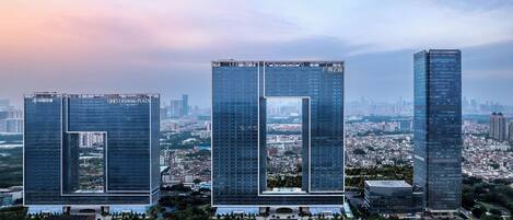 Three high-rise buildings with reflective glass facades, surrounded by greenery and a body of water.
