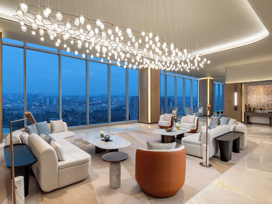 Un lobby amplio con muebles modernos, ventanas grandes con vistas a la ciudad y una lámpara de techo original.
