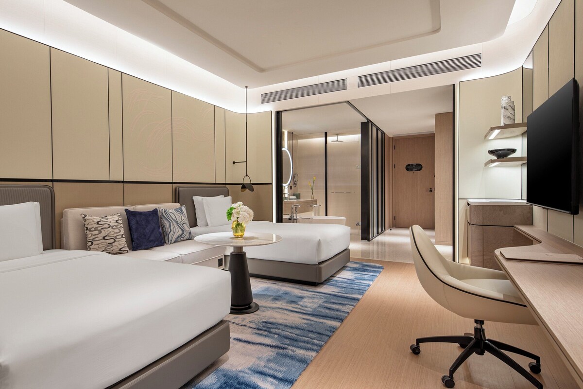 A modern hotel room with two beds, a desk, and a TV.