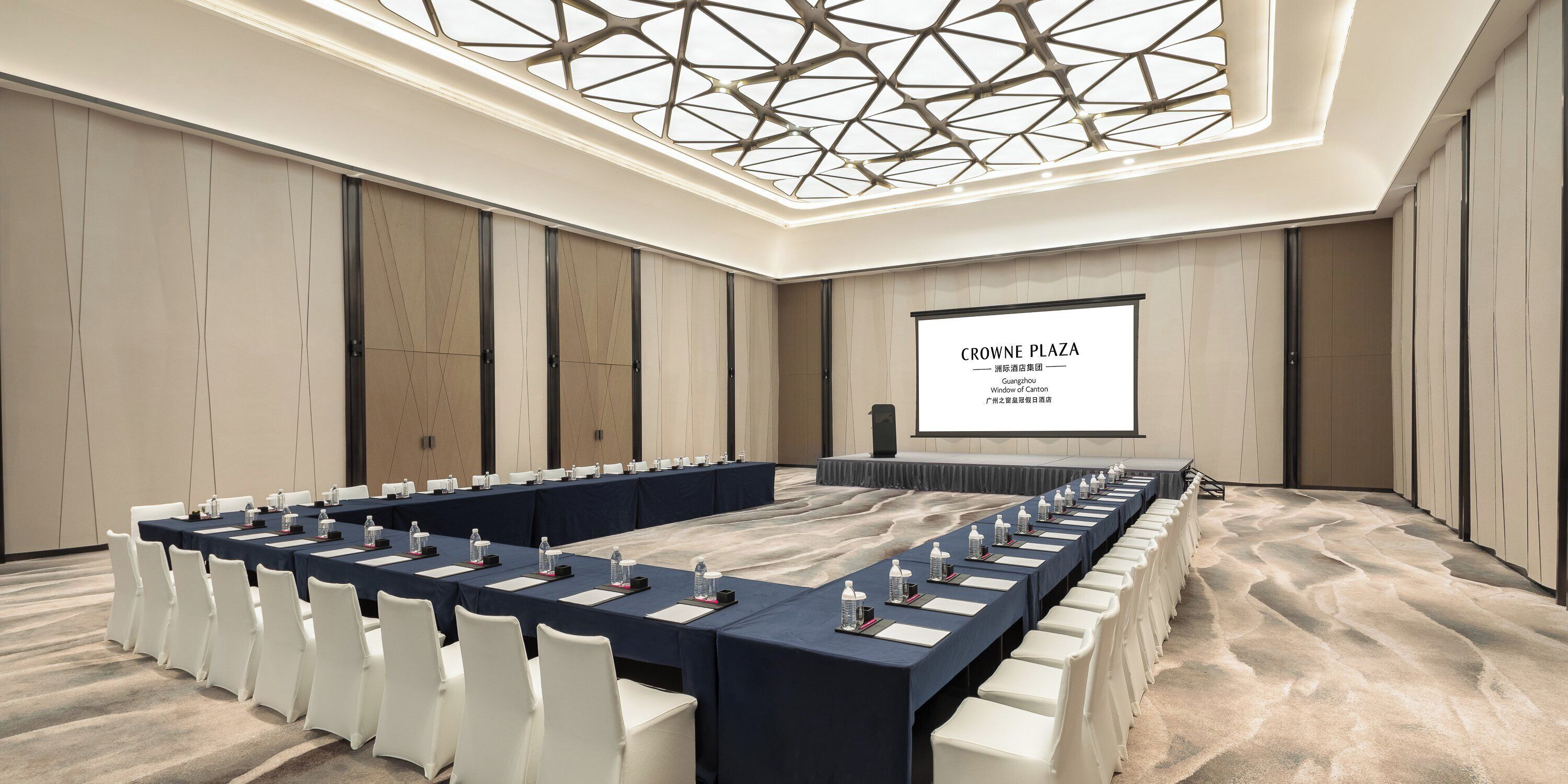 A conference room with a long table, white chairs, and a projector screen displaying 'CROWNE PLAZA'.