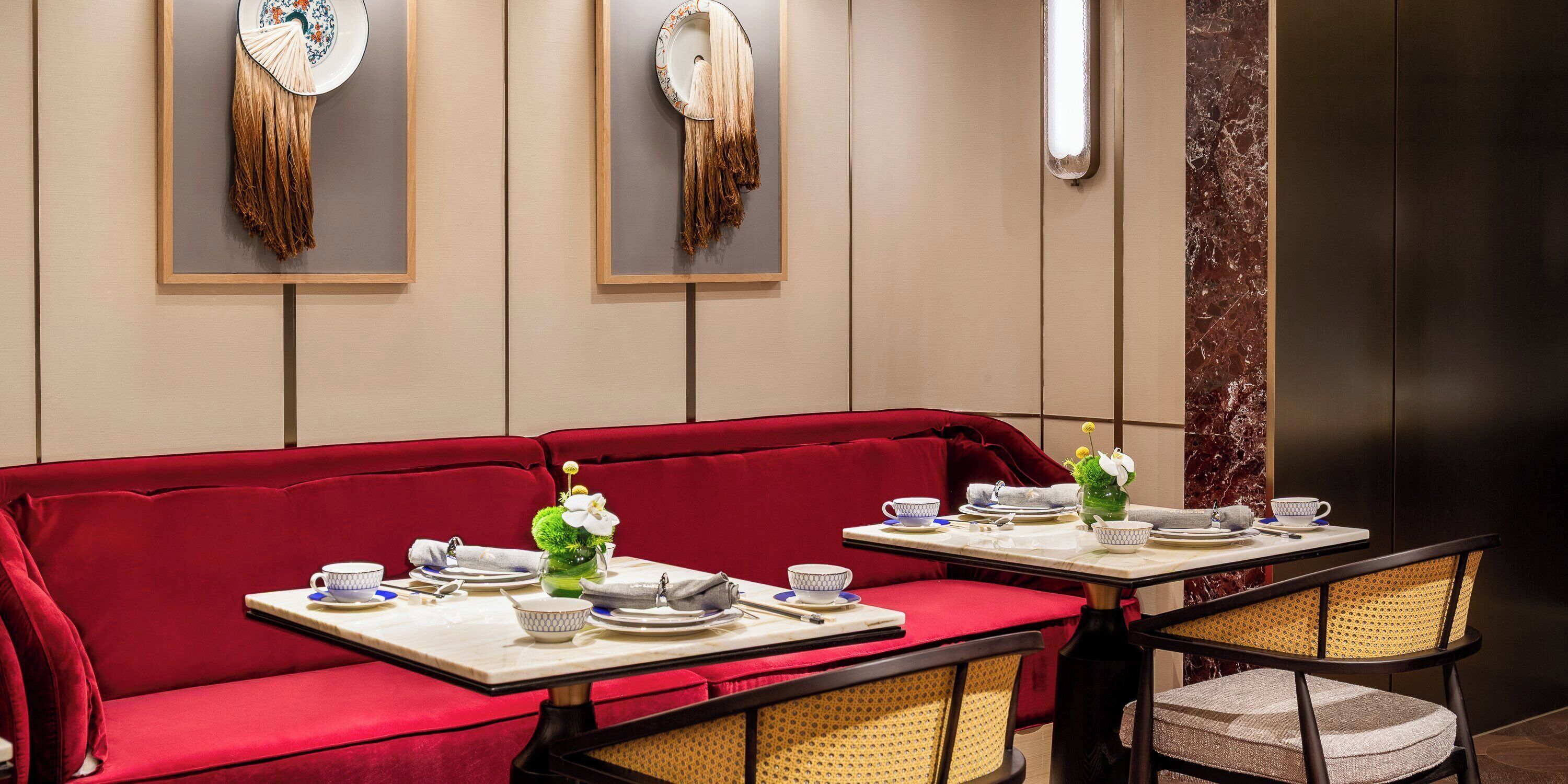 Un área de comedor con un sofá rojo y dos mesas dispuestas con platos, tazones y tazas.