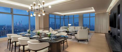 Una habitación de hotel moderna con zona de comedor, un conjunto de sofás y televisión.
