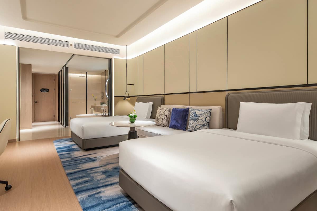 Ein Hotelzimmer mit einem großen Bett, einem Schreibtisch, einem Sessel, einem Fernseher und einem Badezimmer mit Dusche und WC.