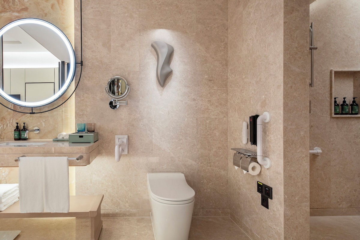Ein modernes Badezimmer mit Marmorwaschtisch, rundem Spiegel, Toilette und Duschbereich.