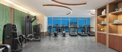 A modern gym with exercise equipment, a patterned floor, and a view of a cityscape through large windows.