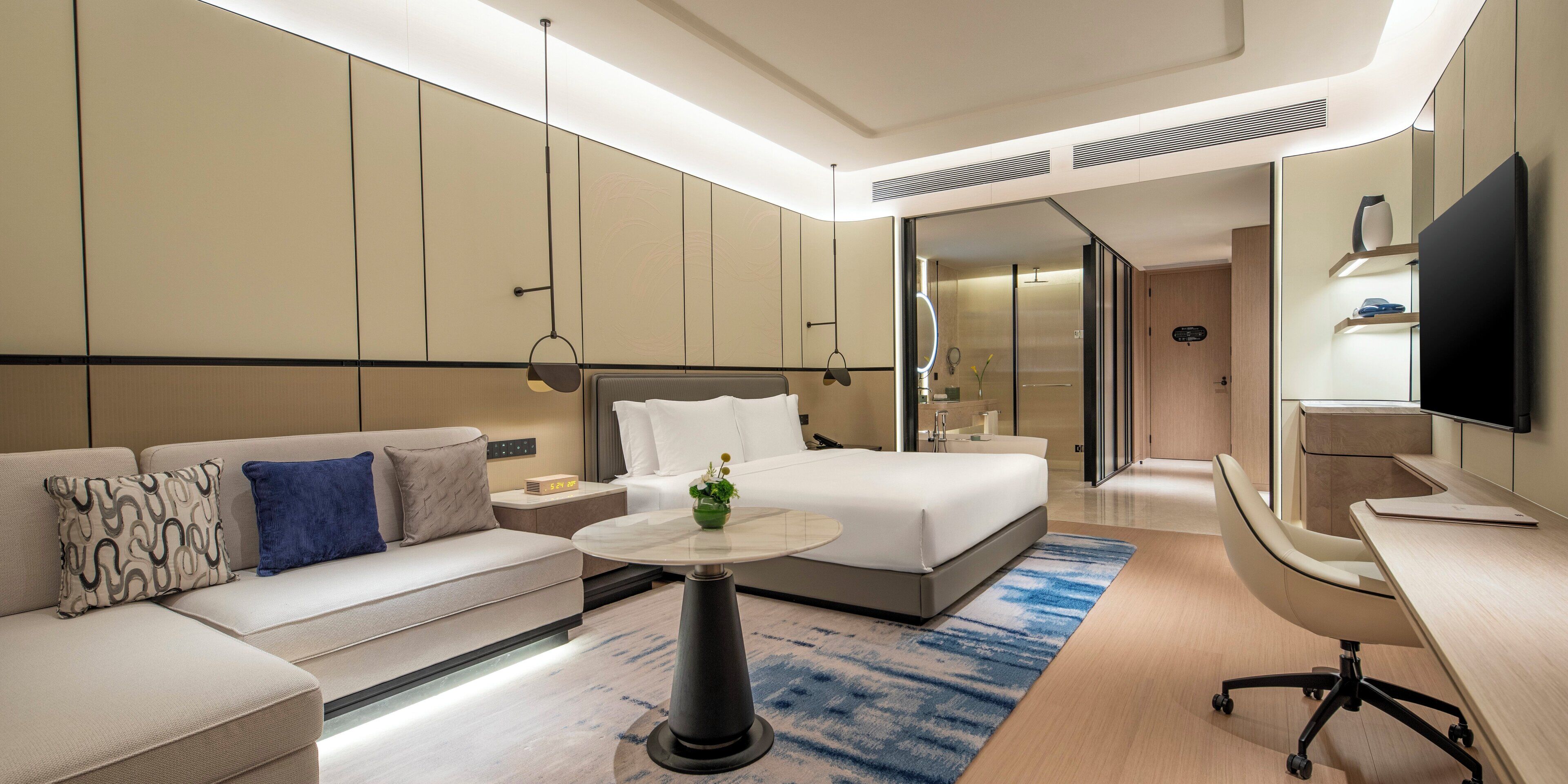 A modern hotel room with a bed, a sofa, a desk, and a television.