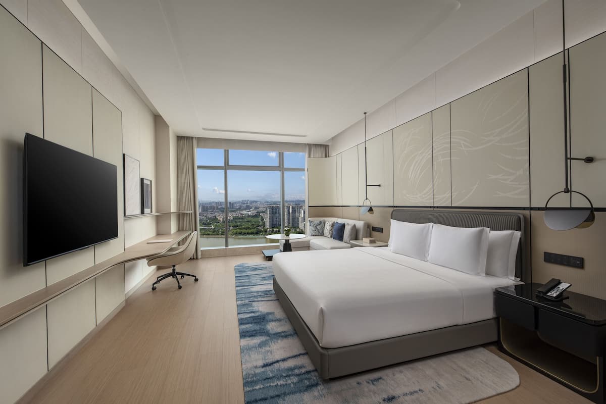 Ein modernes Hotelzimmer mit einem großen Bett, einem Flachbildfernseher, einem Schreibtisch und Blick auf die Stadt.