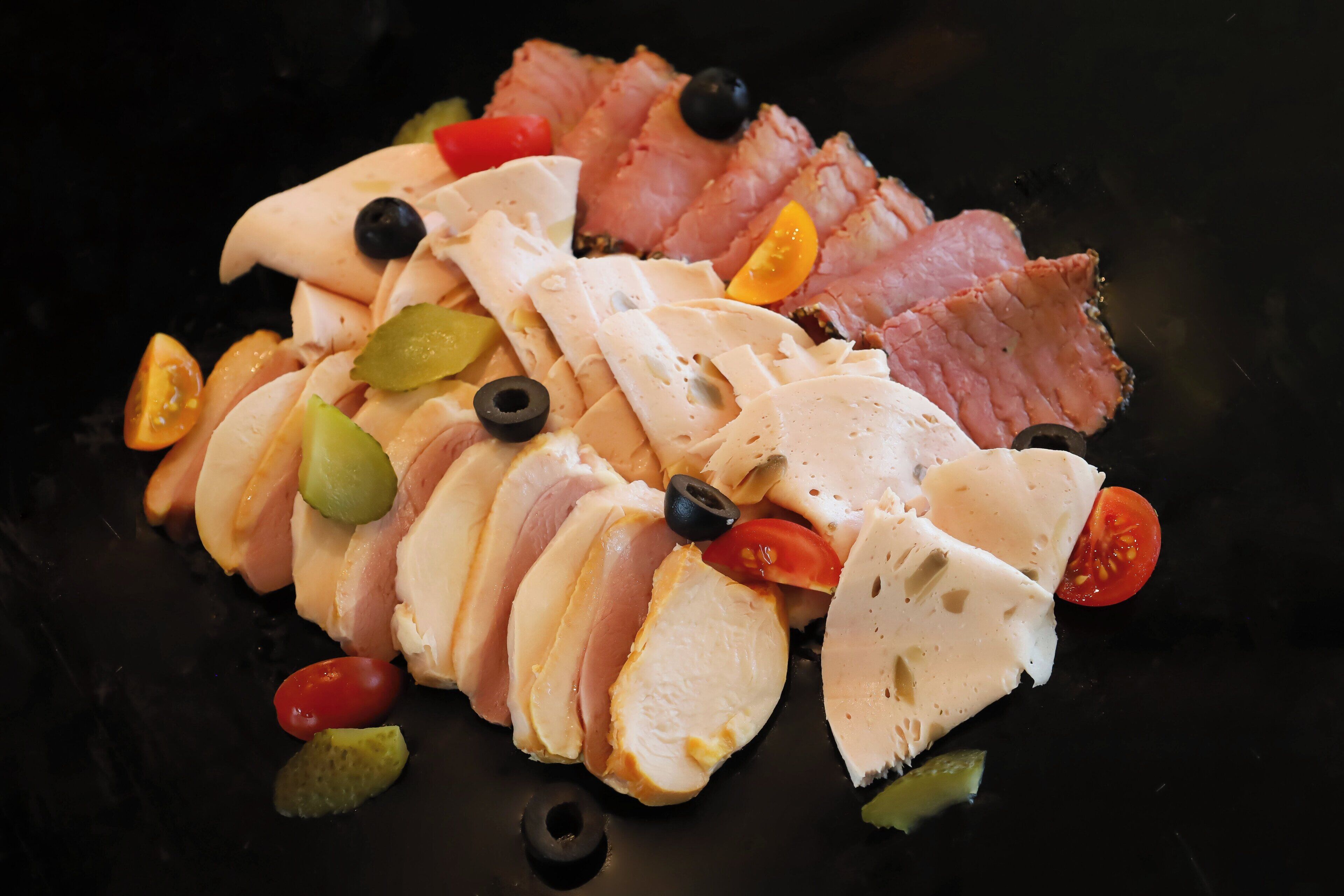 A charcuterie board with sliced meats, cheese, olives, and cherry tomatoes.