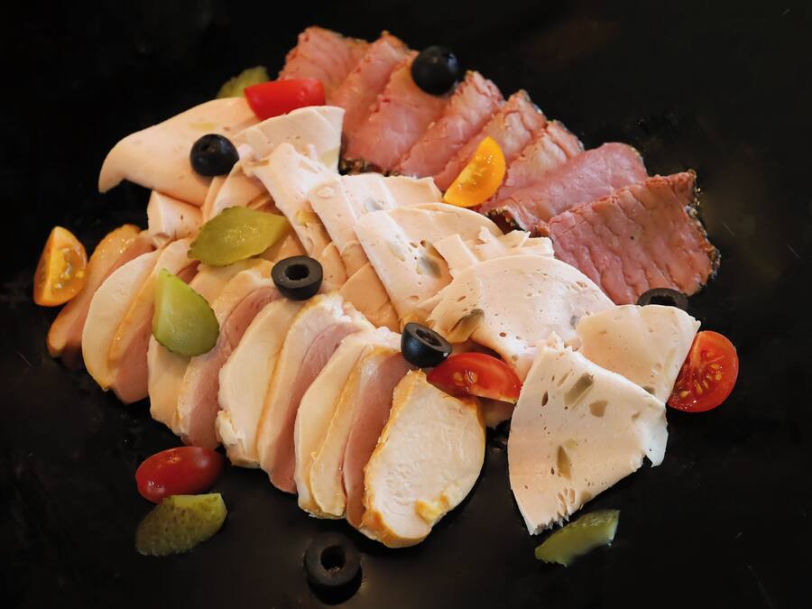 A charcuterie board with sliced meats, cheese, olives, and cherry tomatoes.