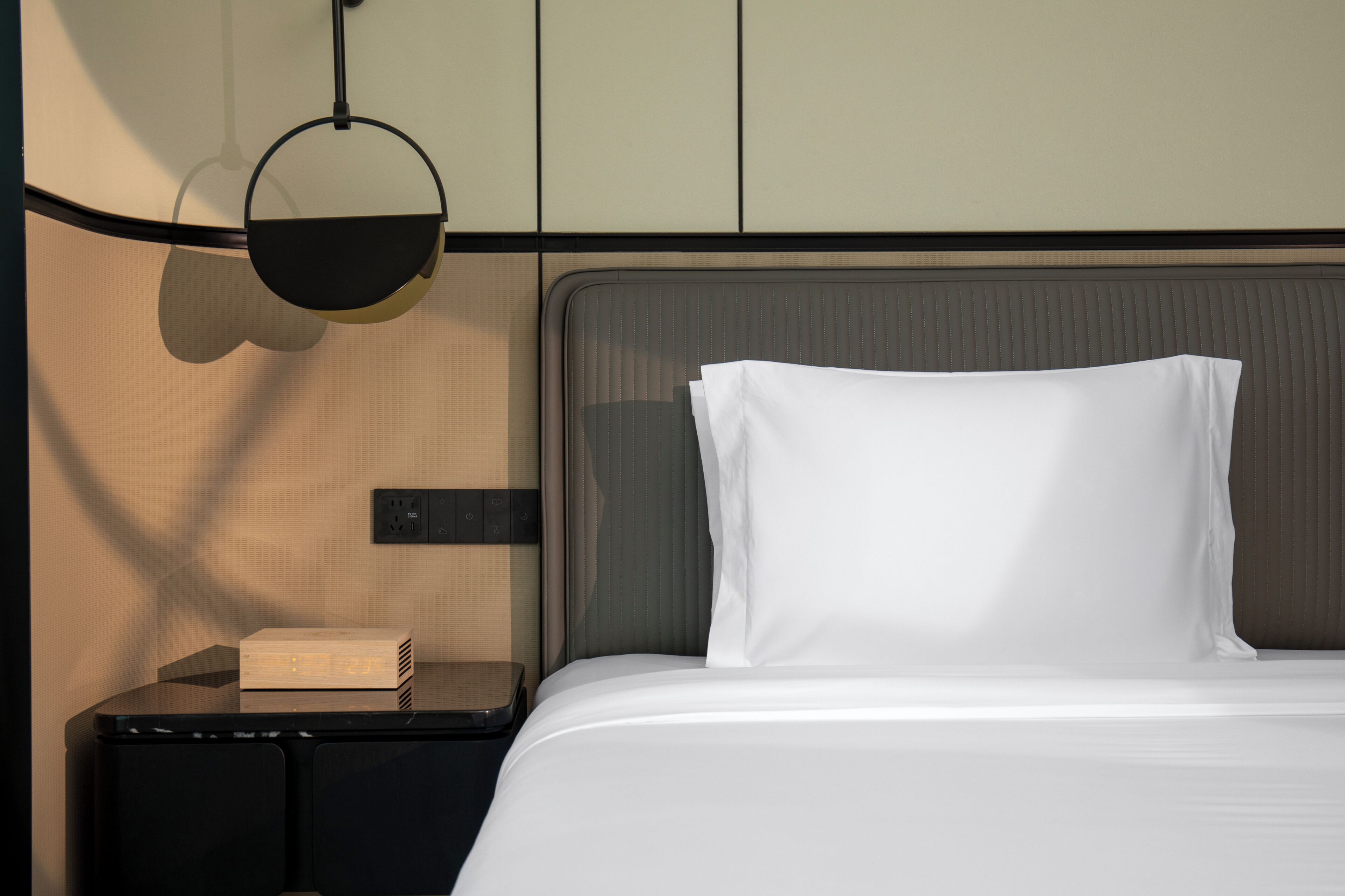 A hotel room with a bed, a bedside table with a lamp, and a wall-mounted power outlet.