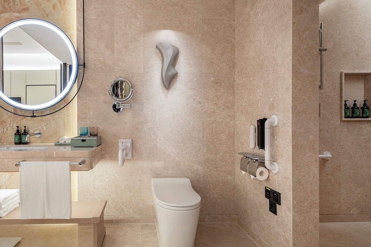 Een moderne badkamer met een marmeren wastafel, een ronde spiegel, een toilet en een douchehoek.