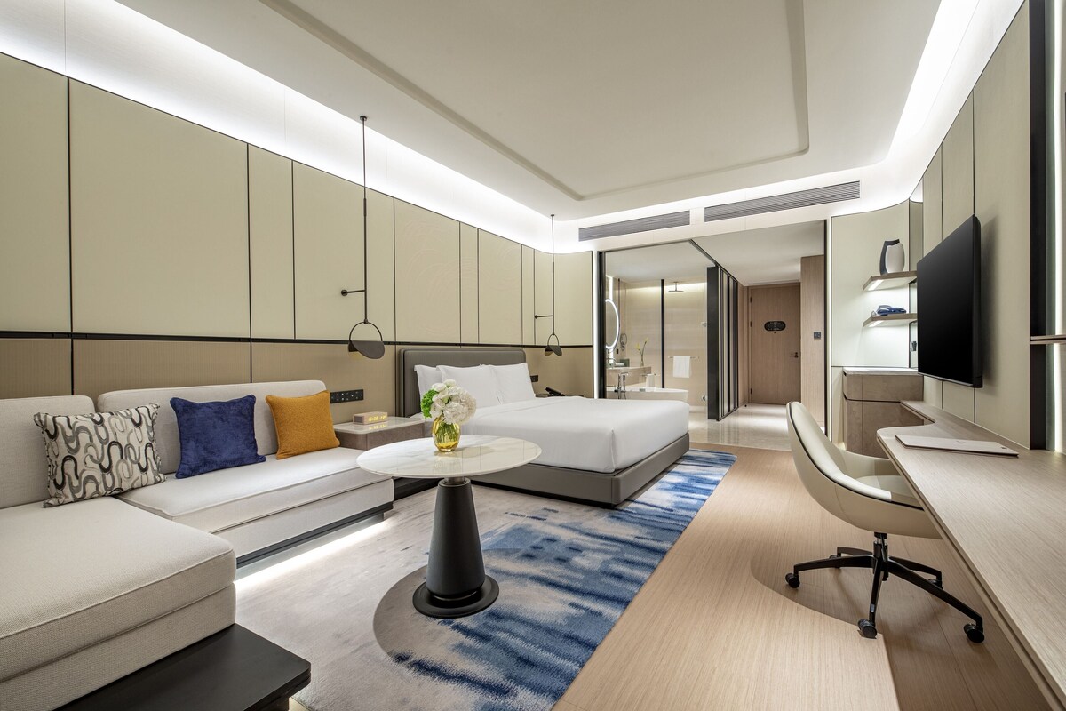 A modern hotel room with a sofa, a bed, a desk, and a television.