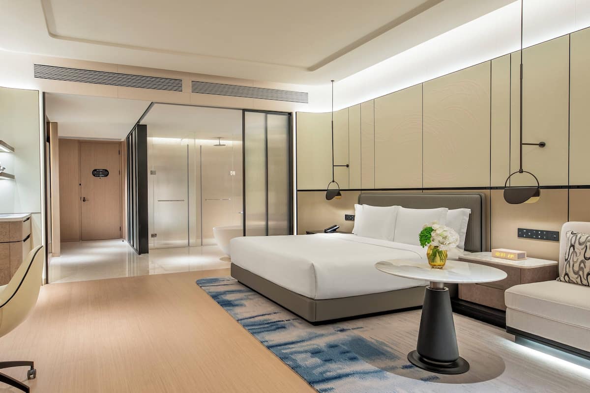 Ein modernes Hotelzimmer mit Bett, Schreibtisch, Fernseher, Sofa und einem kleinen Tisch mit einer Vase.