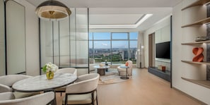 Un salon moderne doté d’une grande fenêtre, d’un coin repas et d’un téléviseur fixé au mur.
