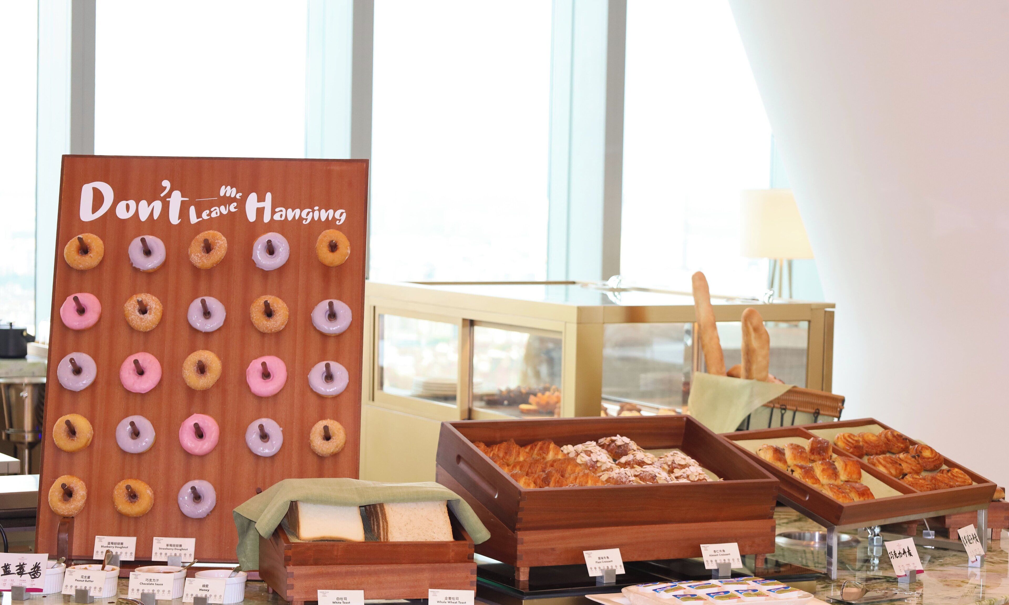 A bakery display with various donuts and pastries, including a sign that reads "Don't Leave Hanging."