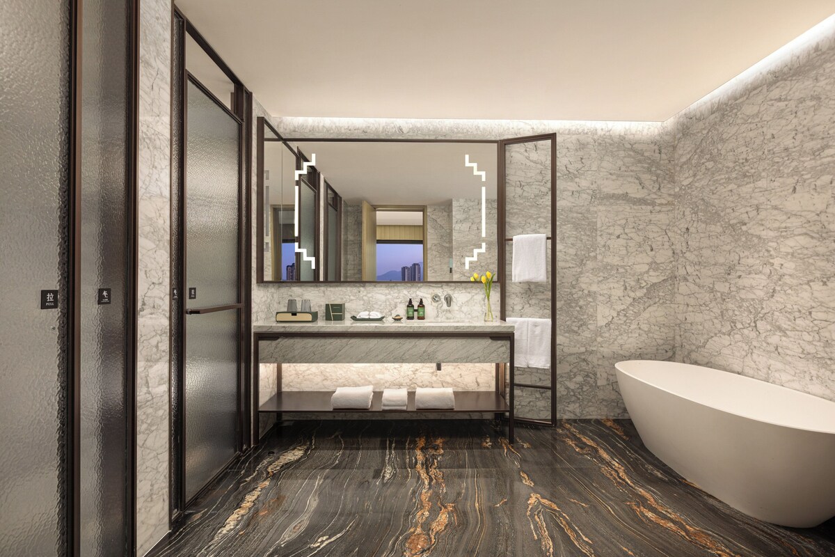 A modern bathroom with a marble vanity, a freestanding bathtub, and a large mirror.