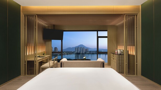 A modern hotel room with a large bed, a desk, and a view of a cityscape and mountains. - Crowne Plaza Putian by IHG (Putian)