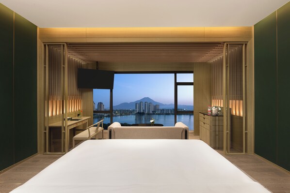 A modern hotel room with a large bed, a desk, and a view of a cityscape and mountains. - Crowne Plaza Putian by IHG (Putian)