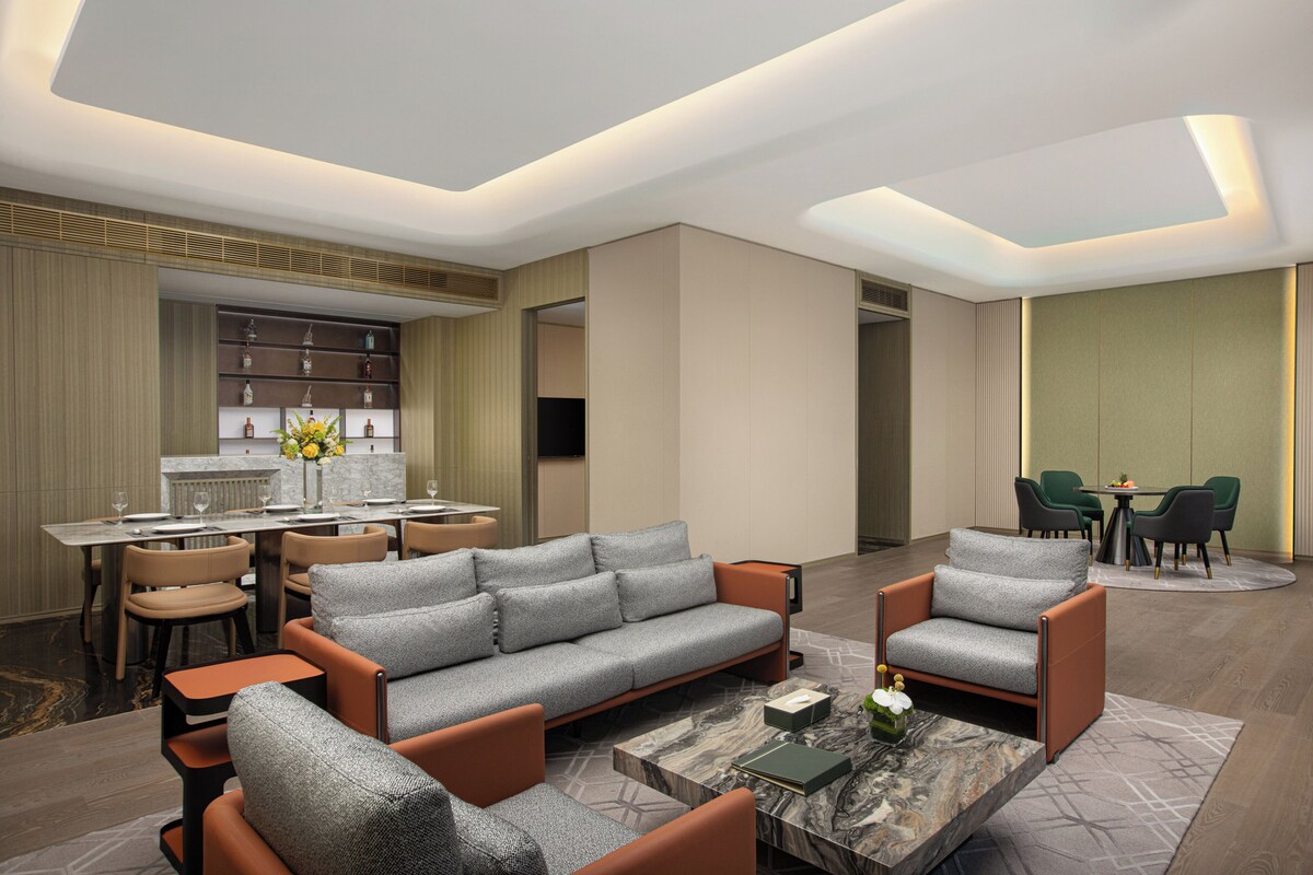 A modern living room with a sofa, armchairs, a coffee table, and a dining area with chairs and a table.