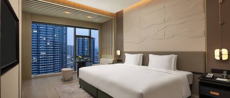 A modern hotel room with a large bed, a desk, and a view of tall buildings.