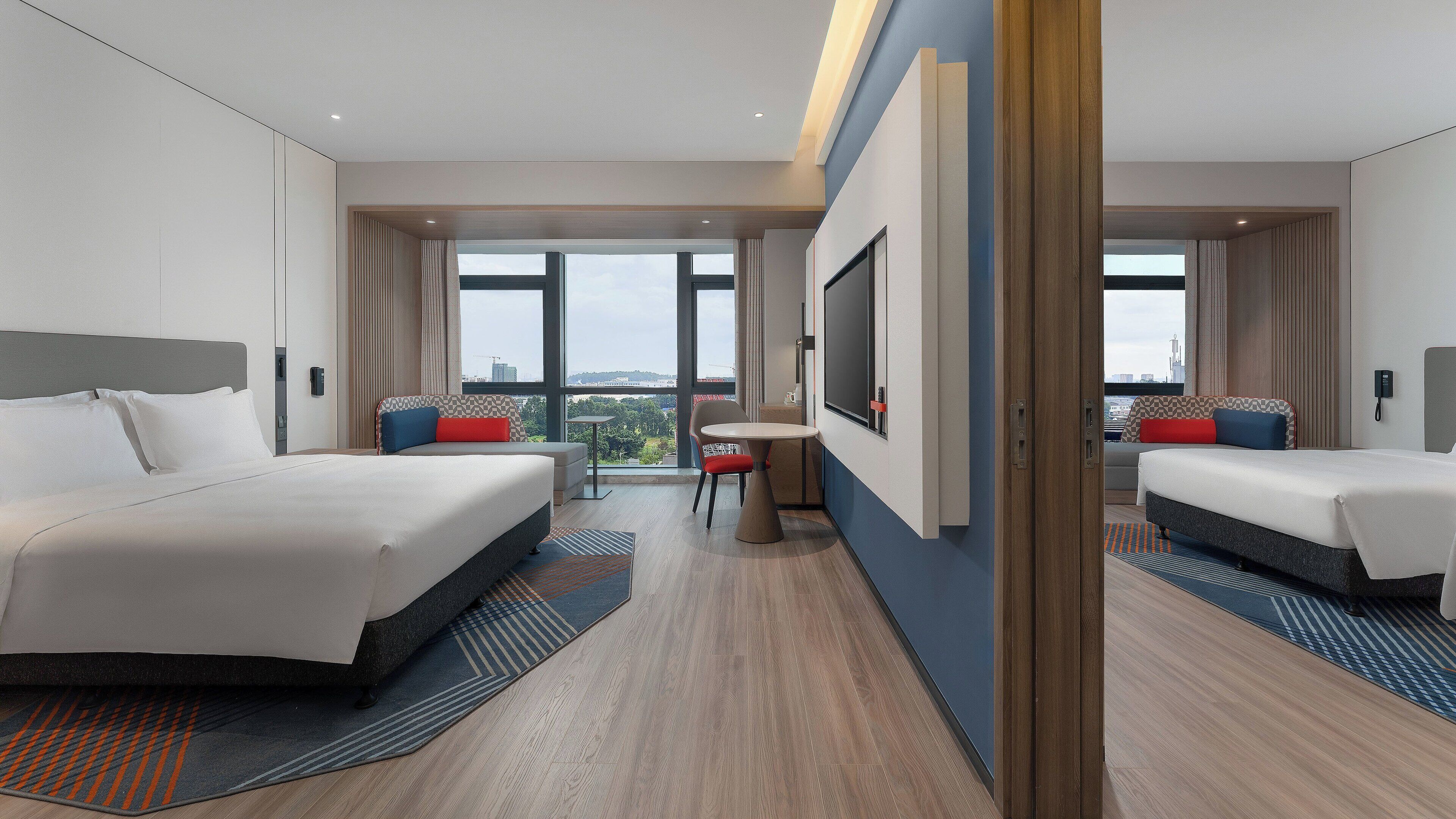 A modern hotel room with two beds, a small table, and a large window offering a city view.