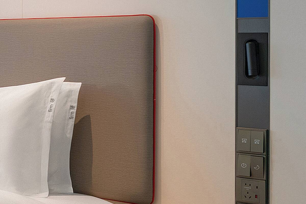 A hotel room with a bed, pillows, and a control panel with buttons and a power outlet.