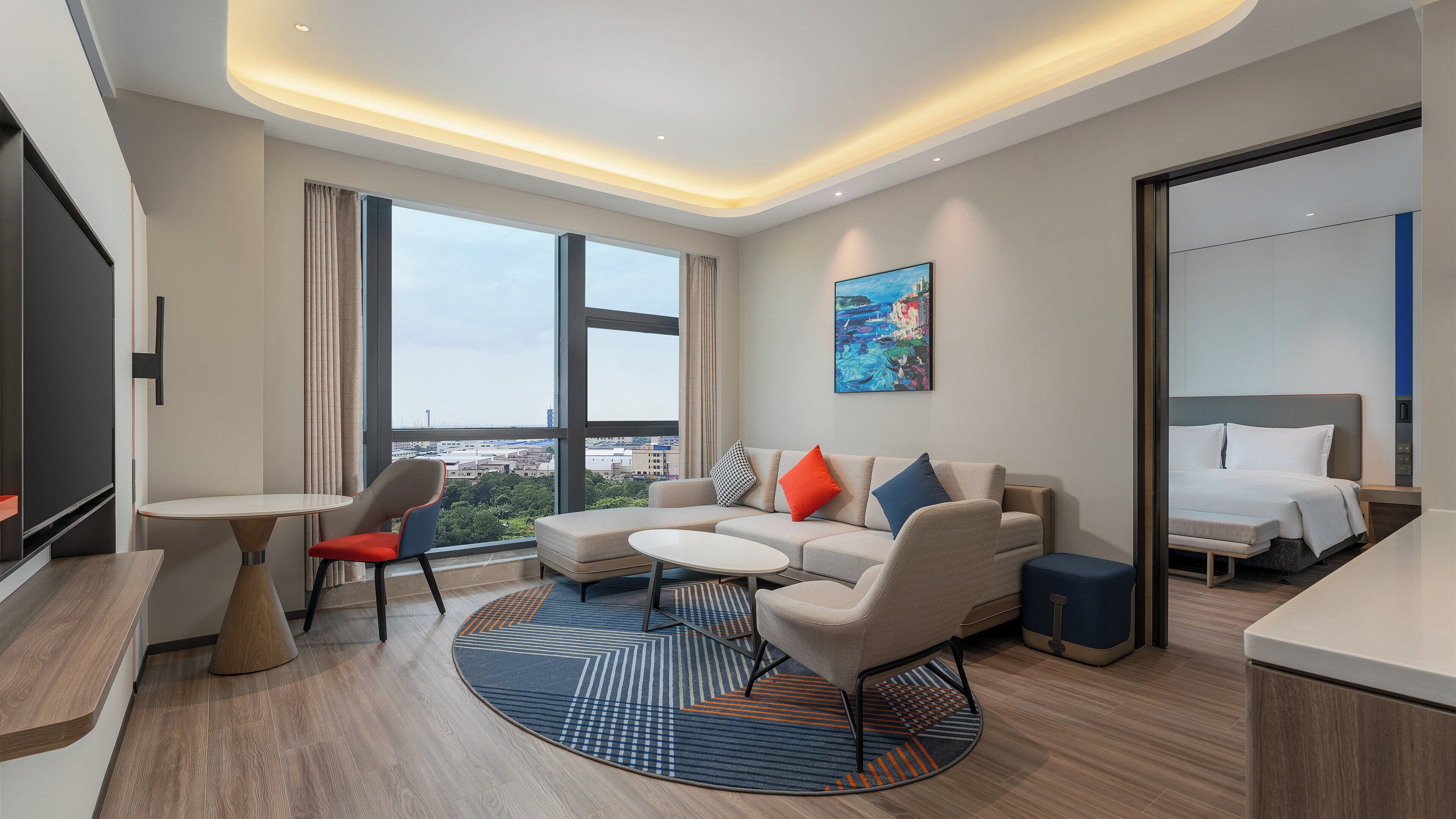 Una habitación de hotel moderna con un ventanal grande, un sofá, una mesita y una cama.