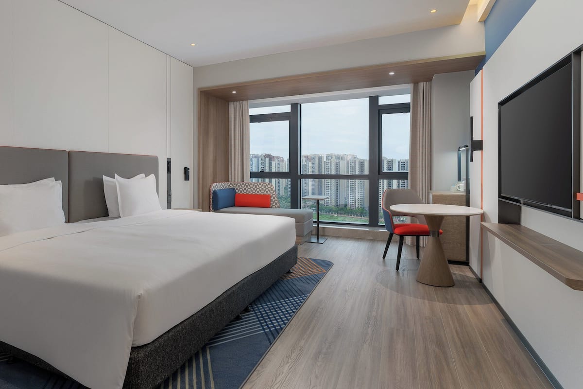 A hotel room with a large bed, a desk, and a view of the city.