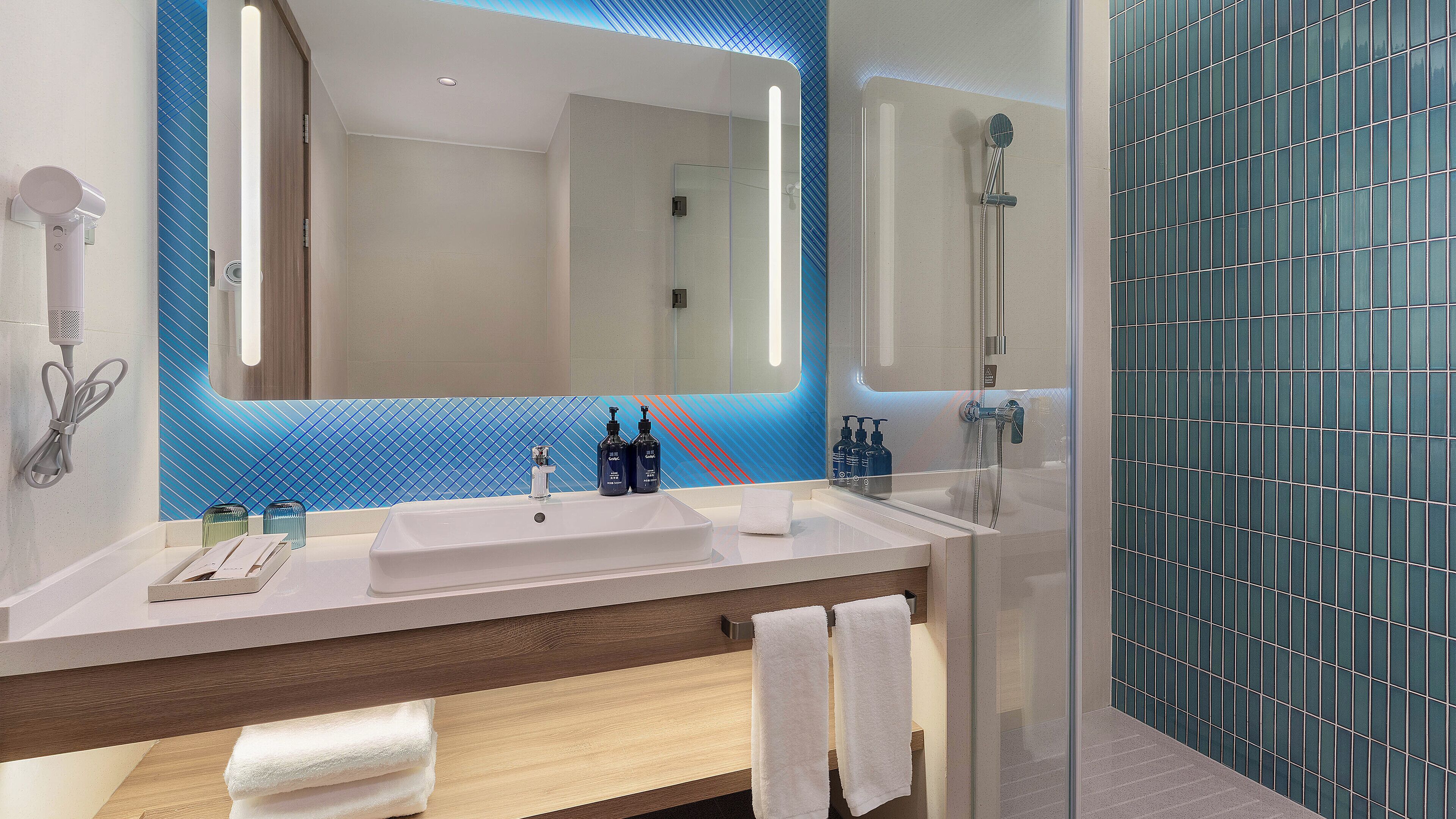 Un baño moderno con un espejo grande, dos lavamanos, una ducha y un perchero para toallas.
