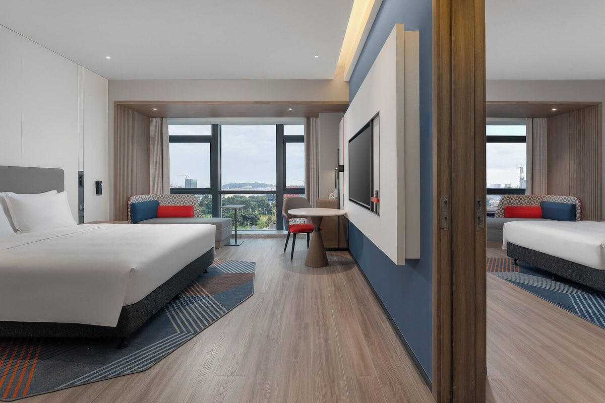 A modern hotel room with two beds, a small table, and a large window offering a city view.