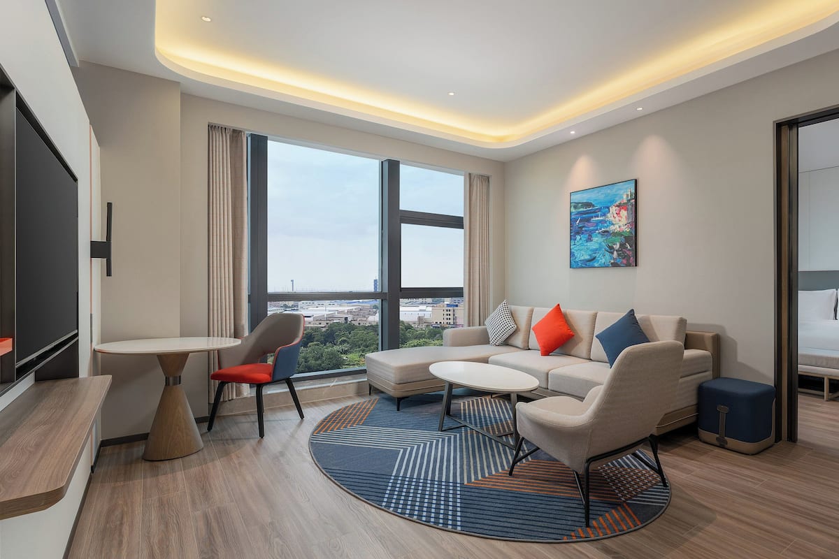 A modern hotel room with a large window, a sofa, a small table, and a bed.
