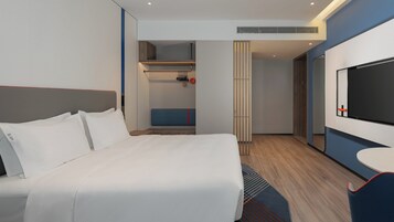 A modern hotel room with a large bed, a TV, and a small seating area.