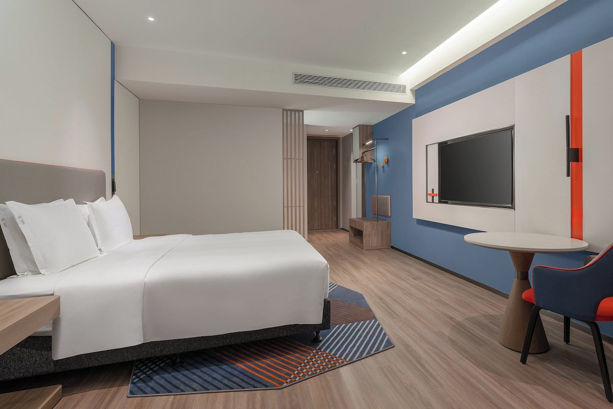 A modern hotel room with a bed, a desk, a chair, and a TV.