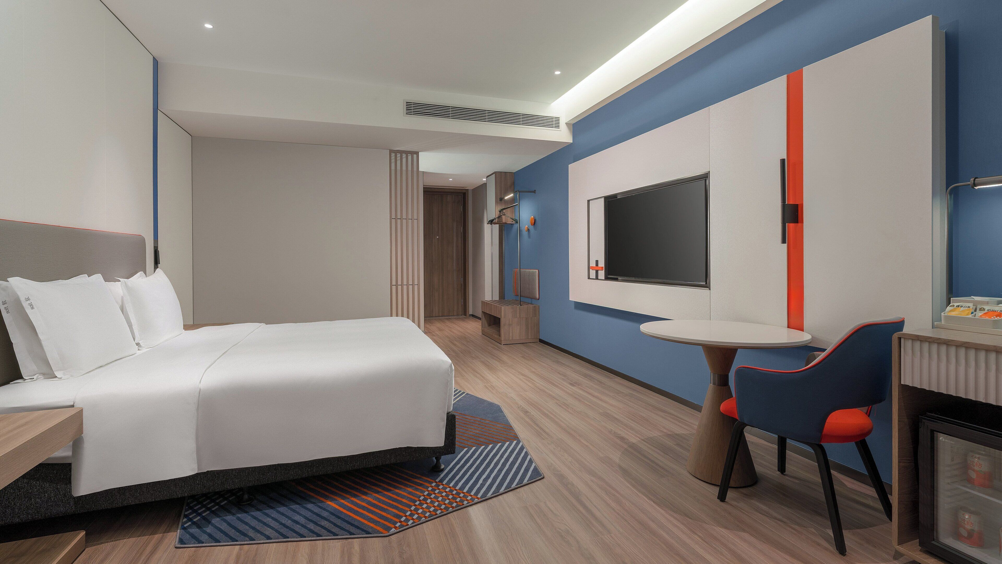 Habitación de hotel con cama, escritorio, silla, televisión y minibar.