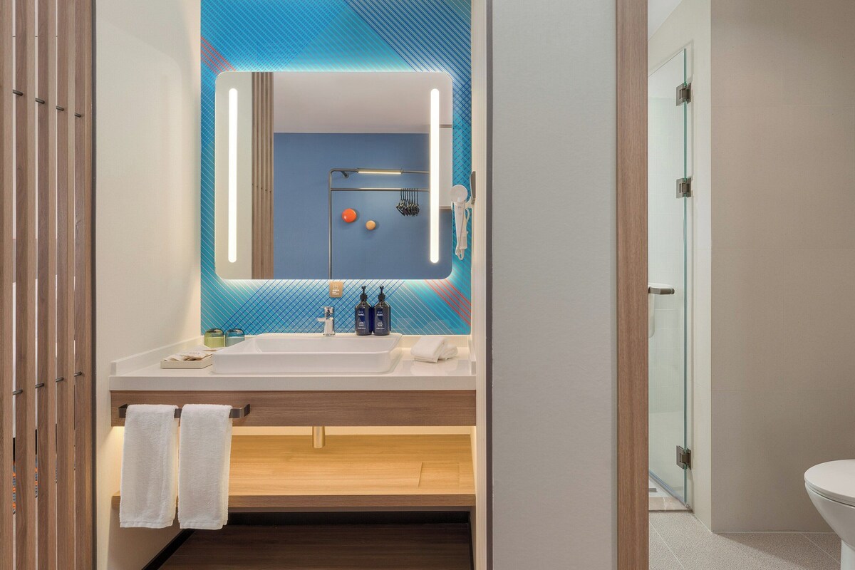 A modern bathroom with a large mirror, a white sink, and a glass shower enclosure.